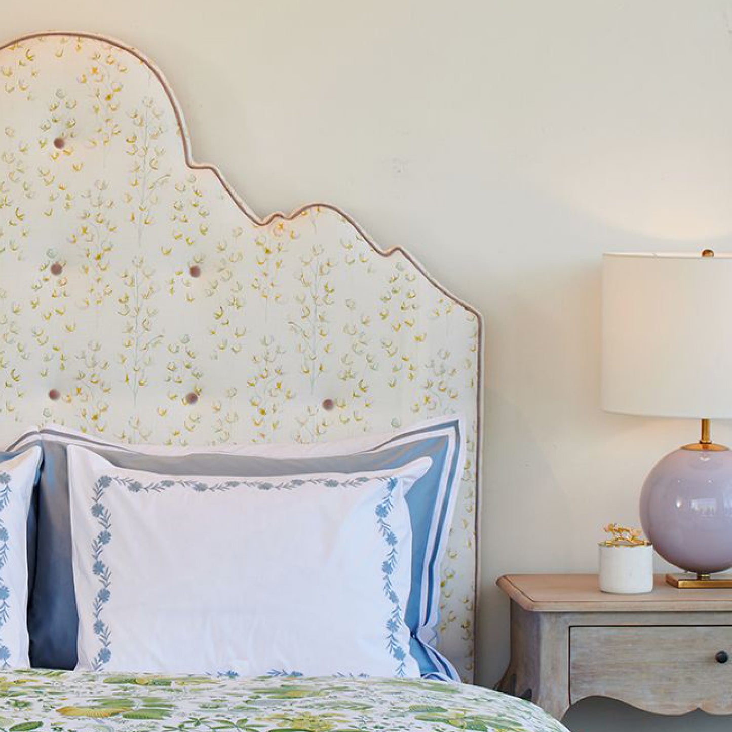 Bedroom with floral headboard, pillows, and nightstand with lamp.