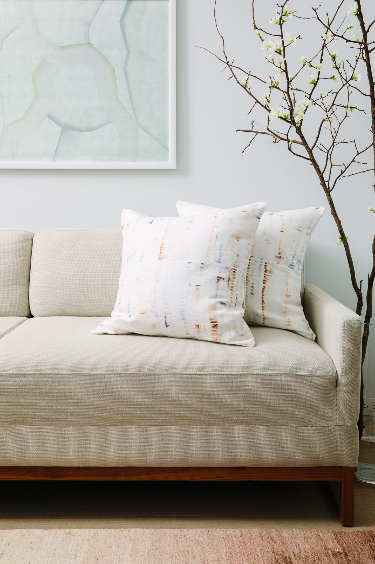 Beige sofa with patterned cushions against a light blue wall with abstract art.