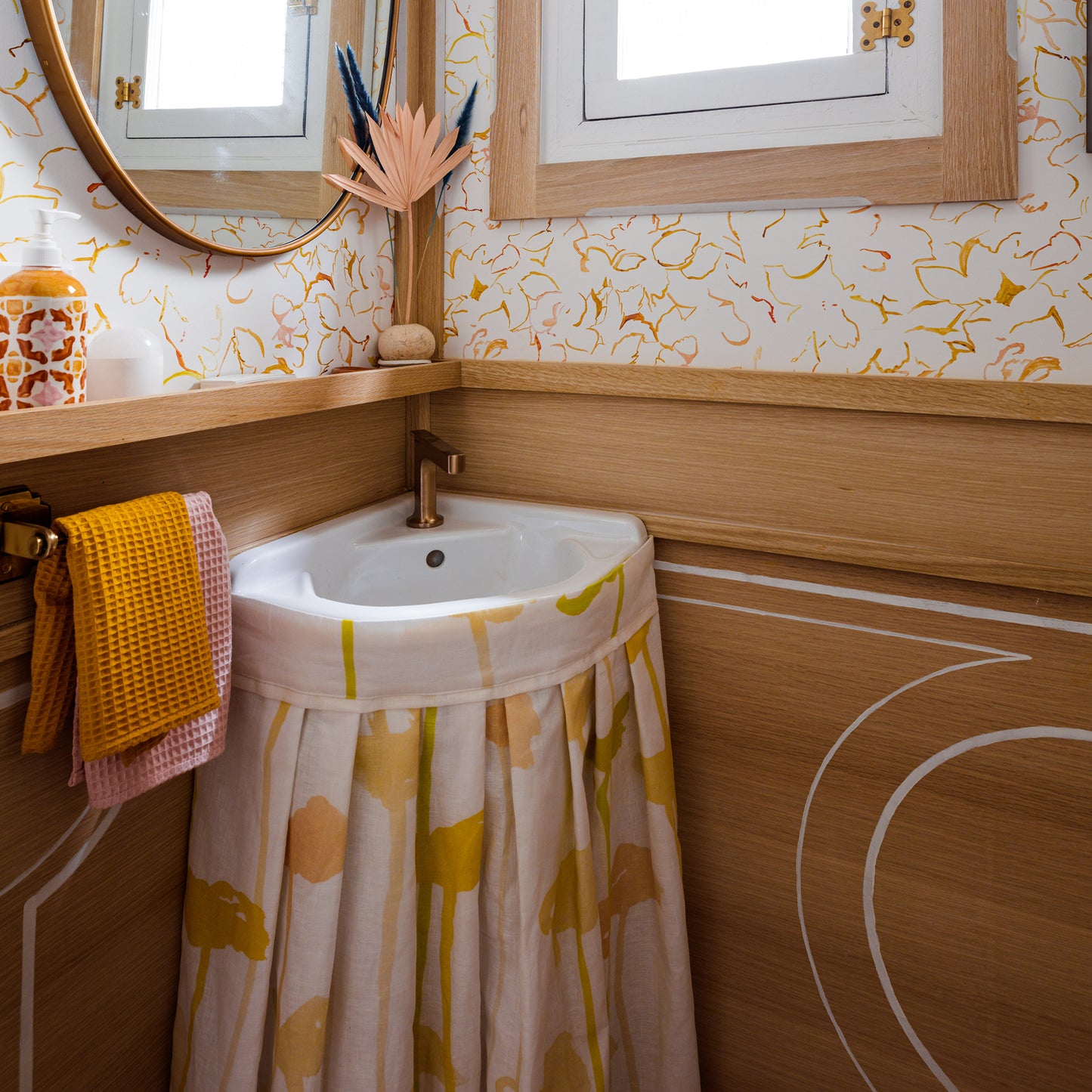 Corner sink with a yellow patterned curtain in a bathroom with wooden walls and decorative elements.