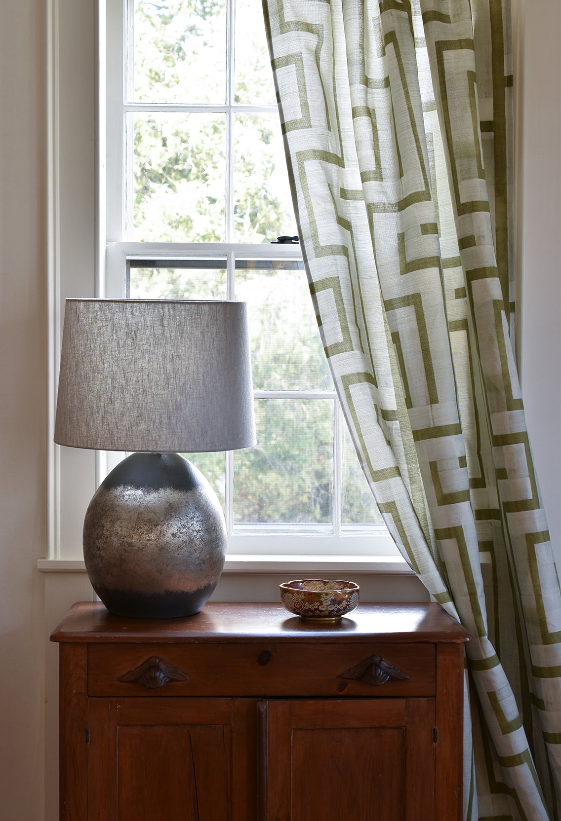 Decorative lamp on a wooden cabinet with a window and patterned curtain in the background