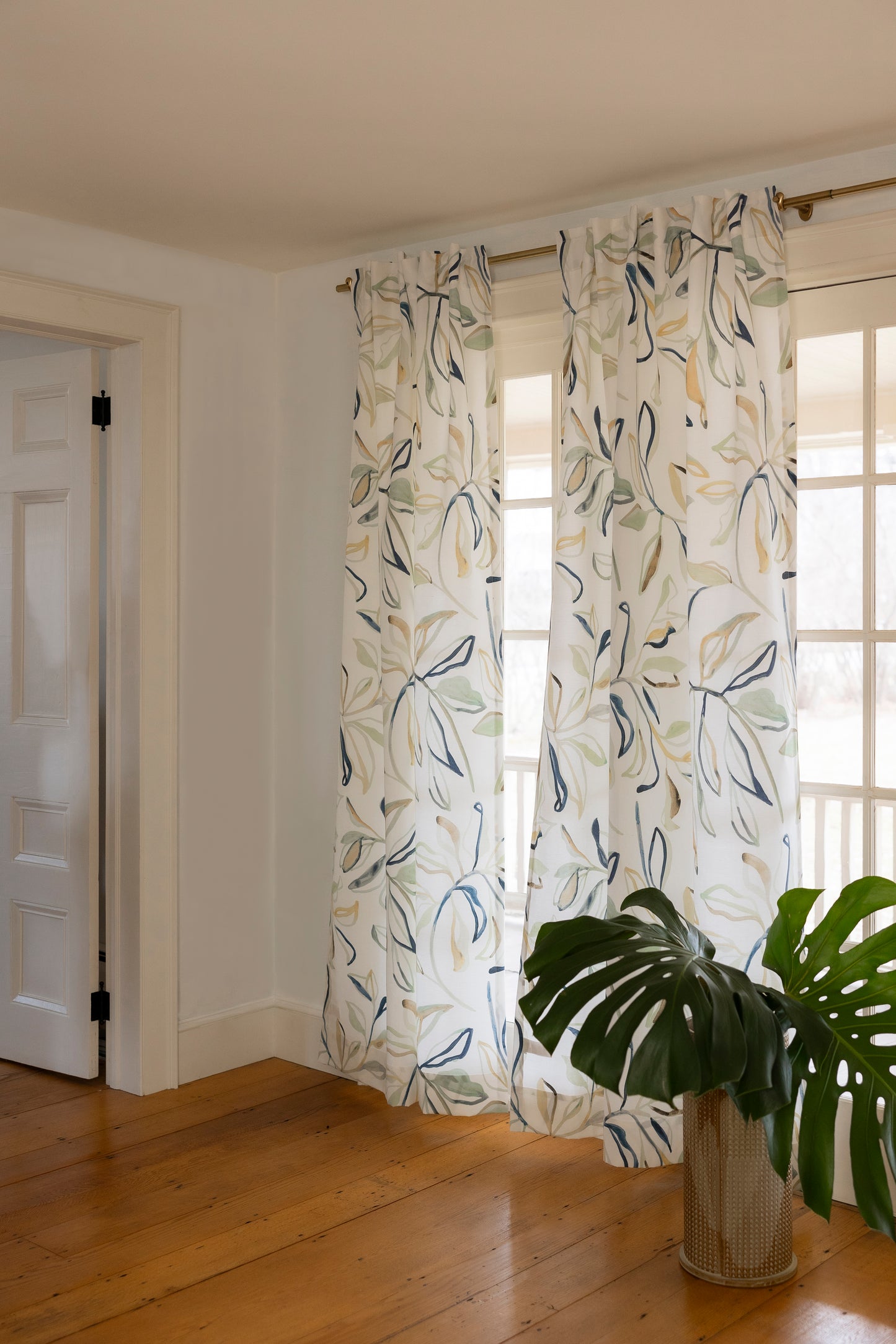 Floral patterned curtains in a room with wooden flooring and a plant.