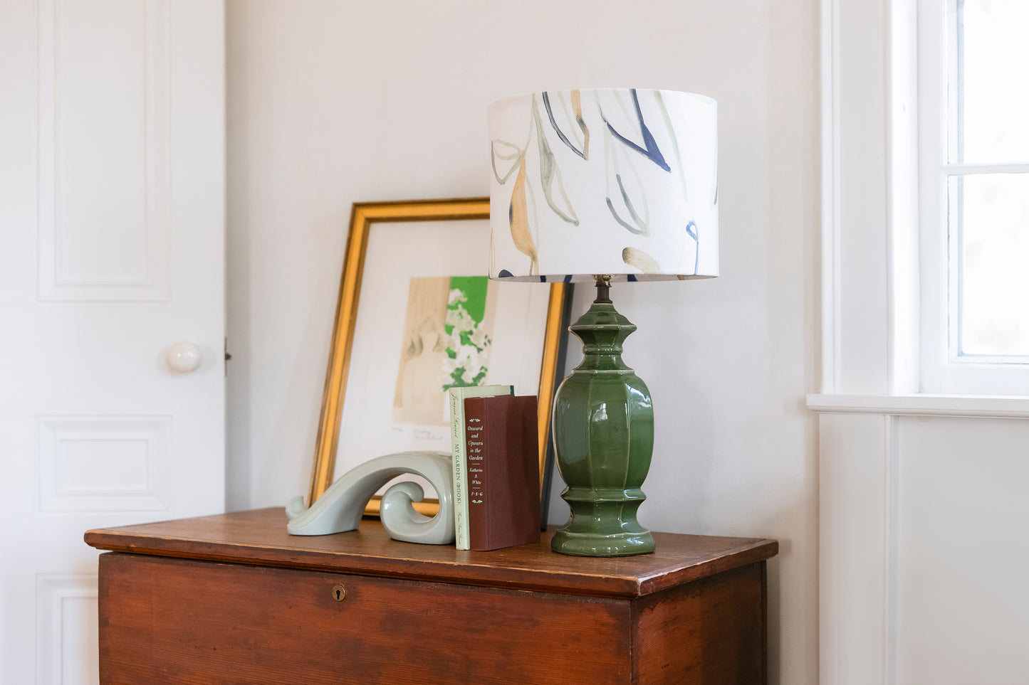 Green lamp on a wooden surface with a framed picture and decorative items in a room.