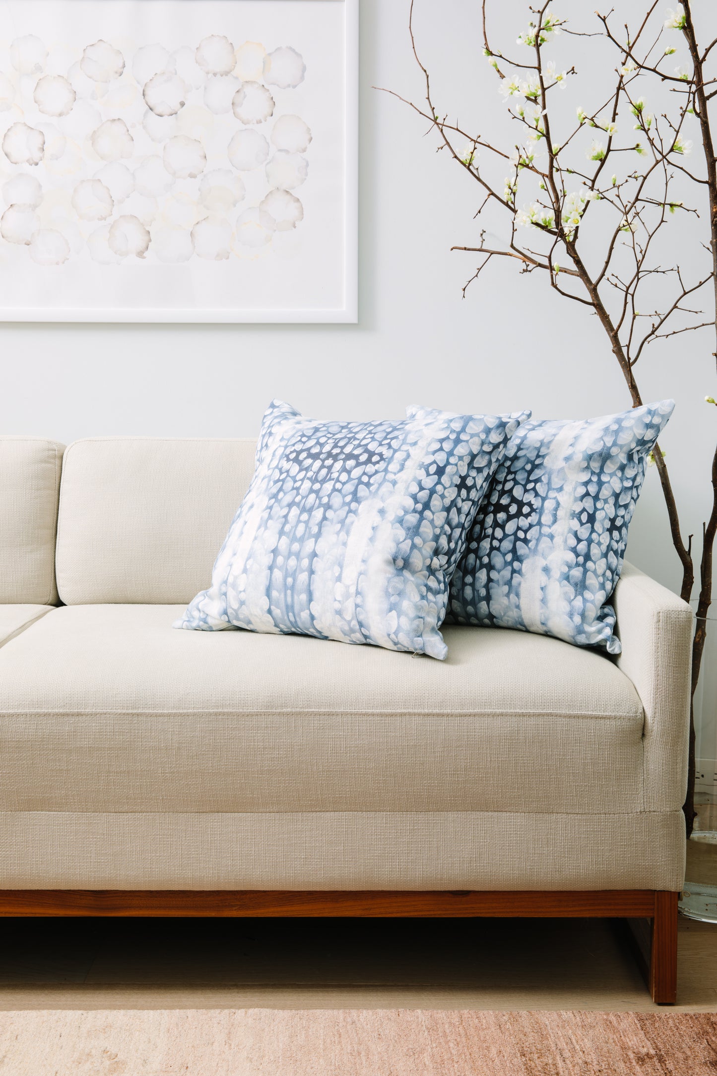 Beige sofa with blue patterned pillows in a room with a plant and framed artwork.