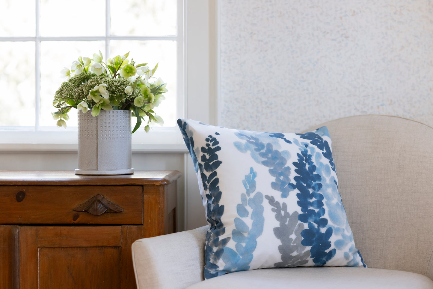 Decorative pillow with floral pattern on a sofa next to a wooden side table with a plant.