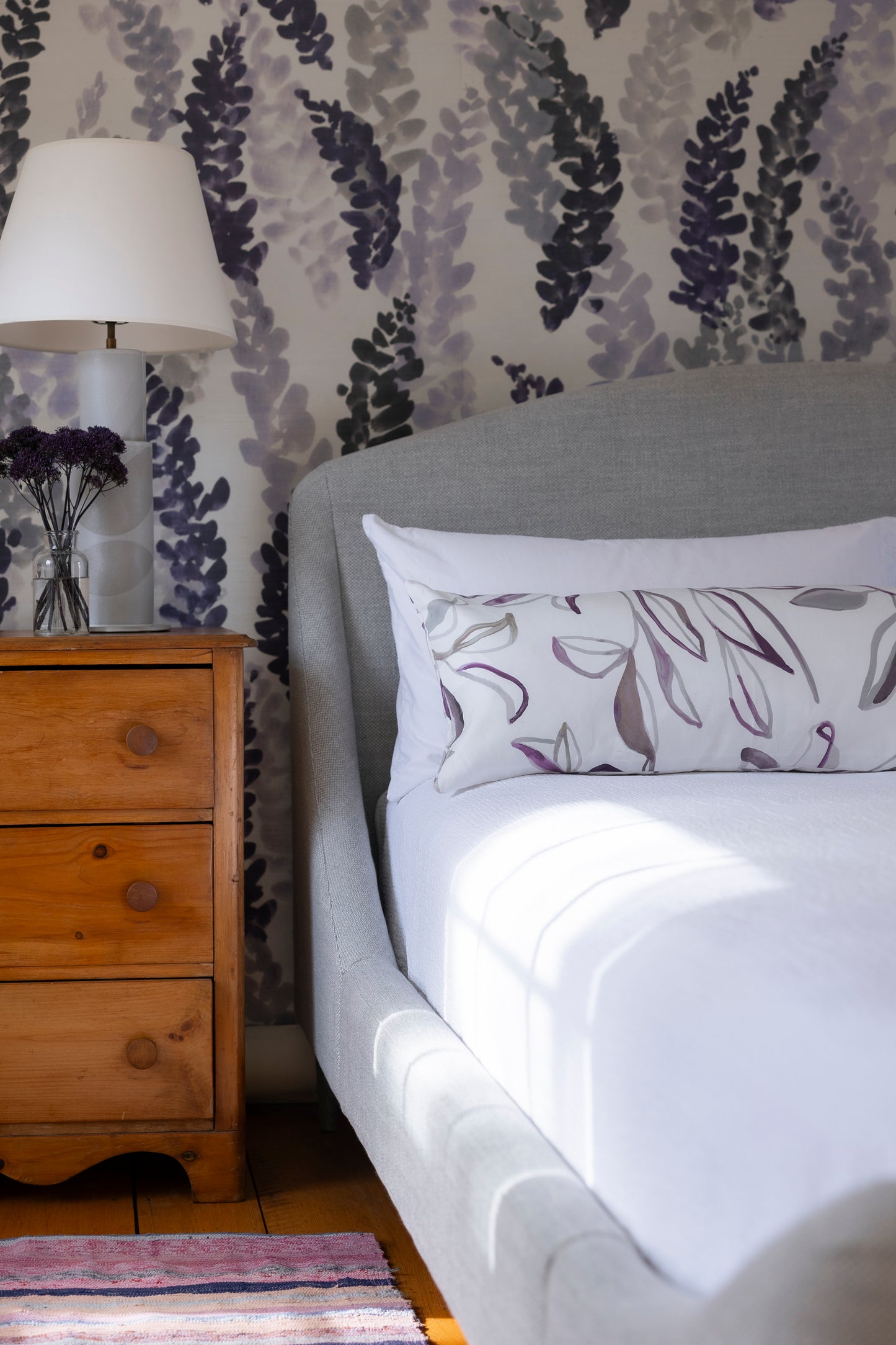 Bedroom with floral wallpaper, wooden nightstand, and bed with patterned pillow.