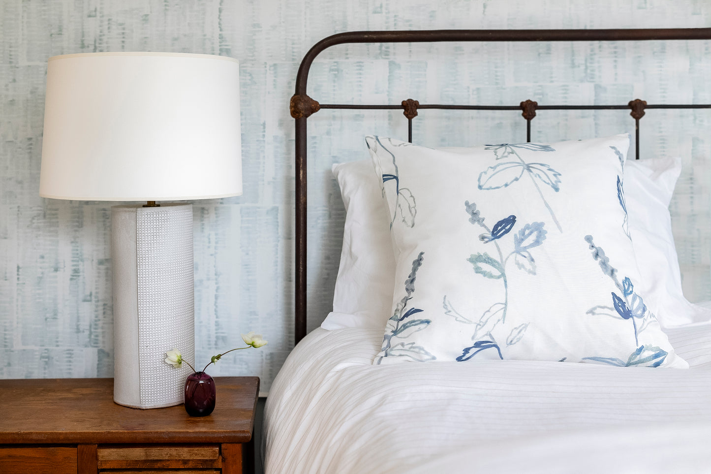 Bedroom with floral-patterned pillows on a bed, nightstand with lamp, and textured wall.