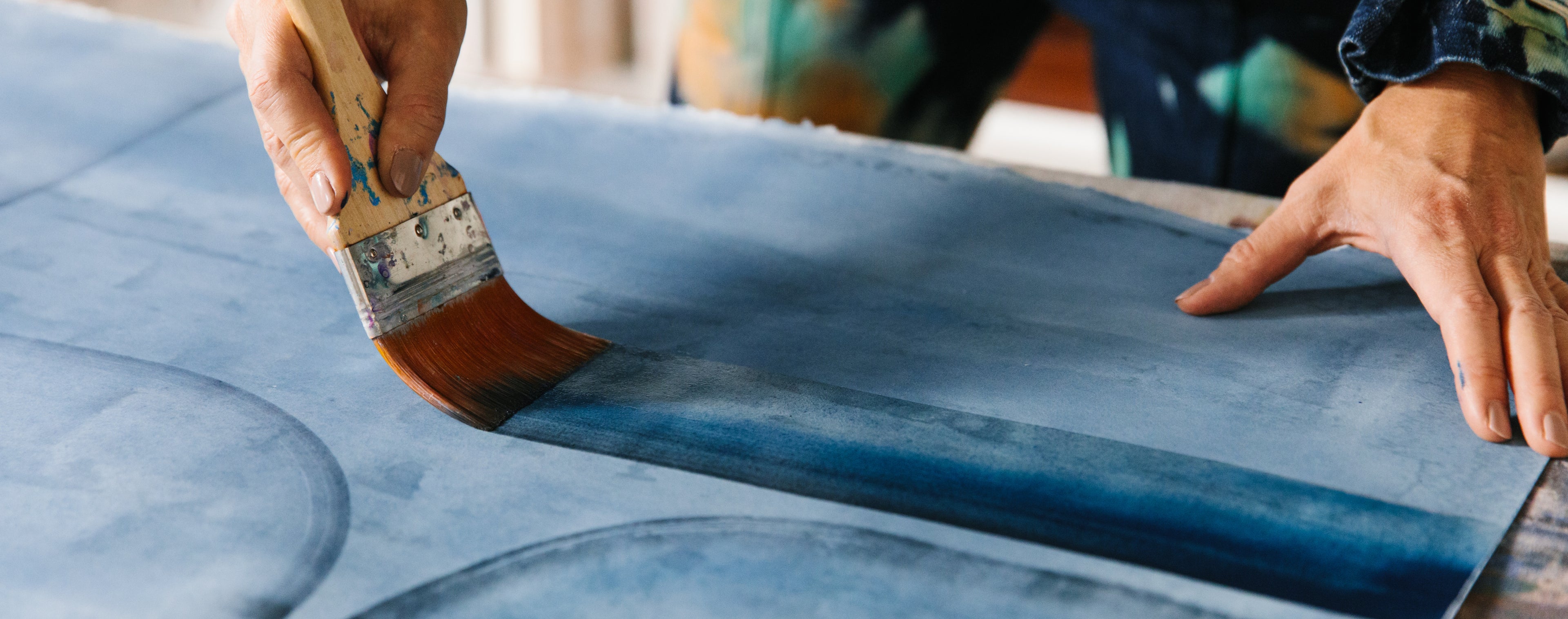 Person applying blue paint to paper with a brush
