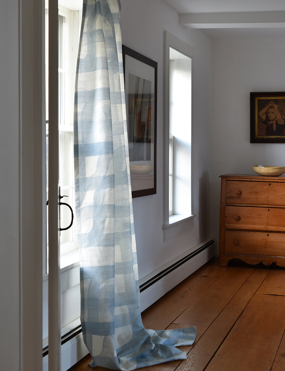 Room with wooden floor, light blue linear patterned curtain, and framed pictures on the wall.