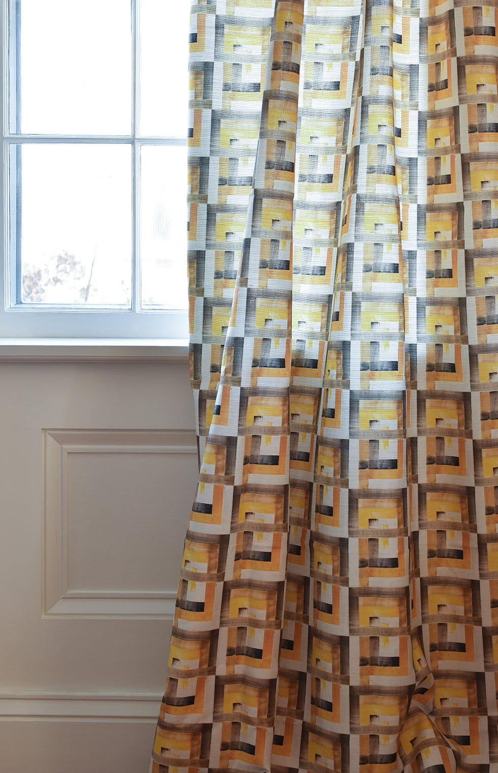 Patterned curtain in front of a window with a neutral wall background