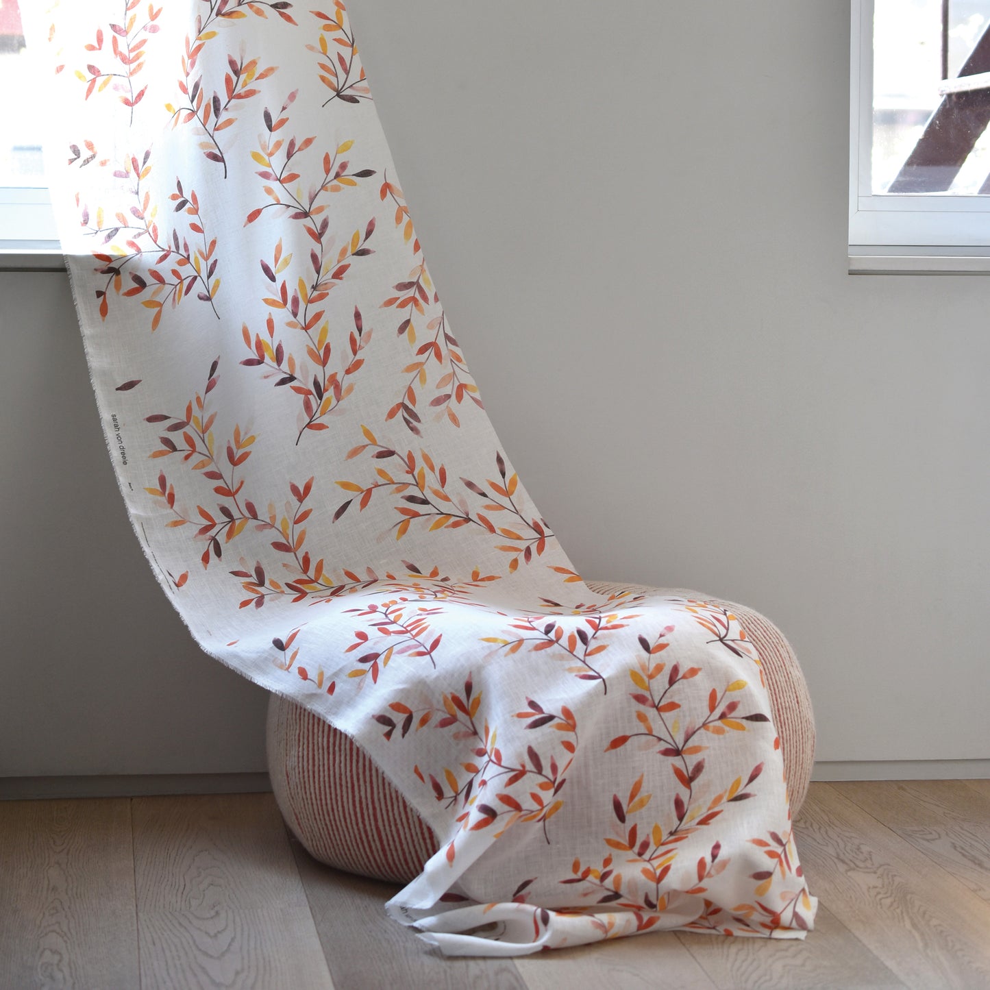 Chair draped with a white blanket featuring autumn leaf pattern in a minimalistic room.