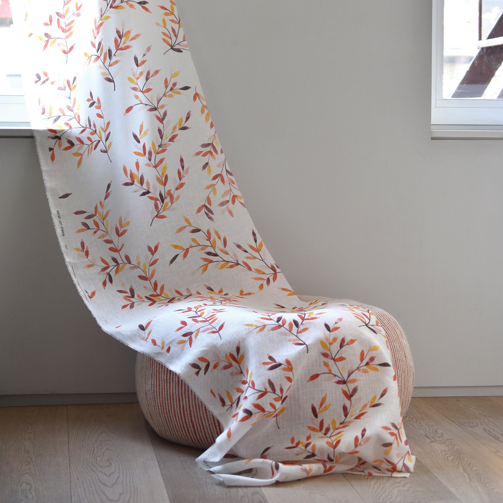Chair draped with a white blanket featuring autumn leaf pattern in a minimalistic room.