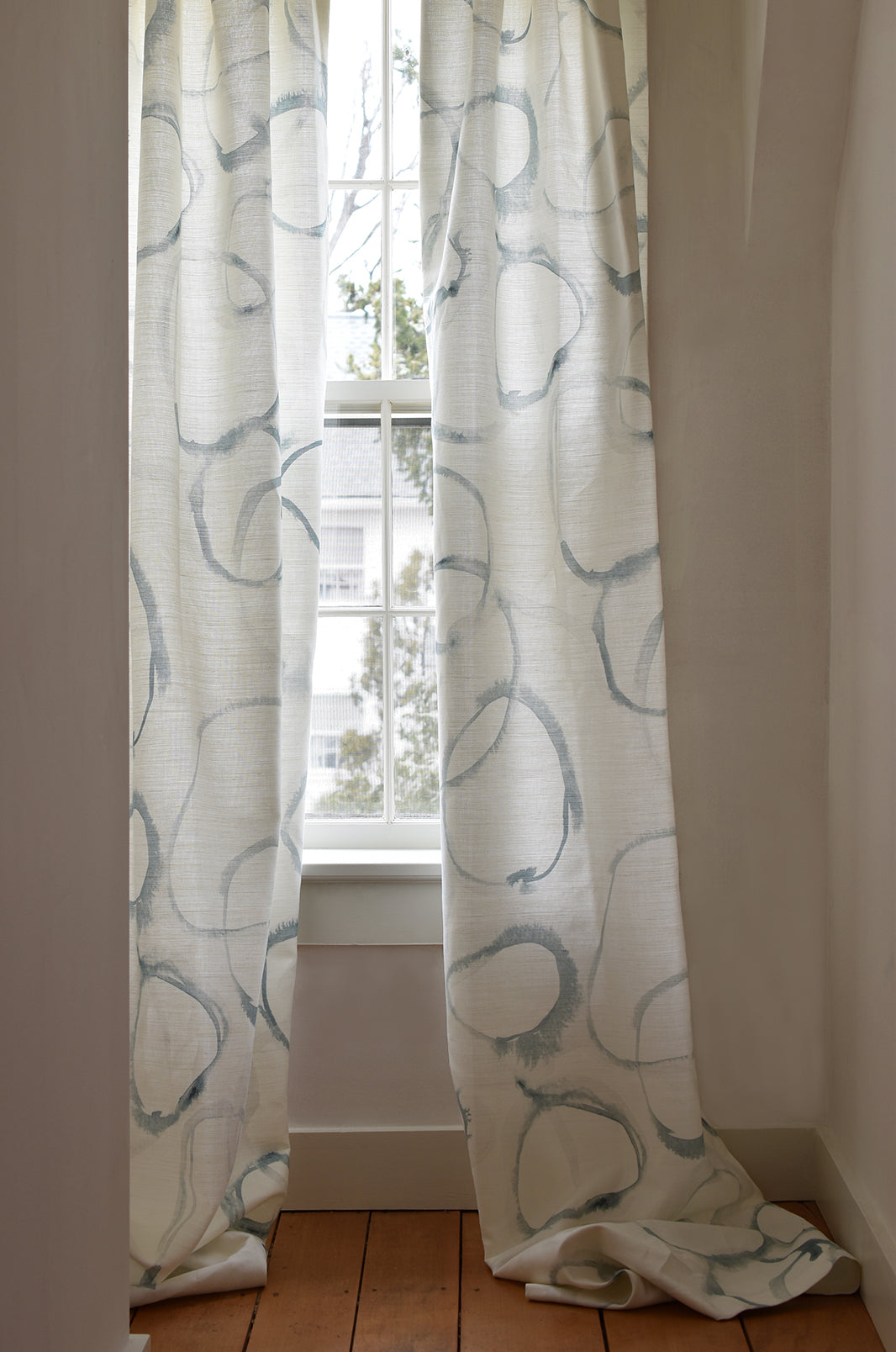 White curtains with blue patterns hanging in front of a window.