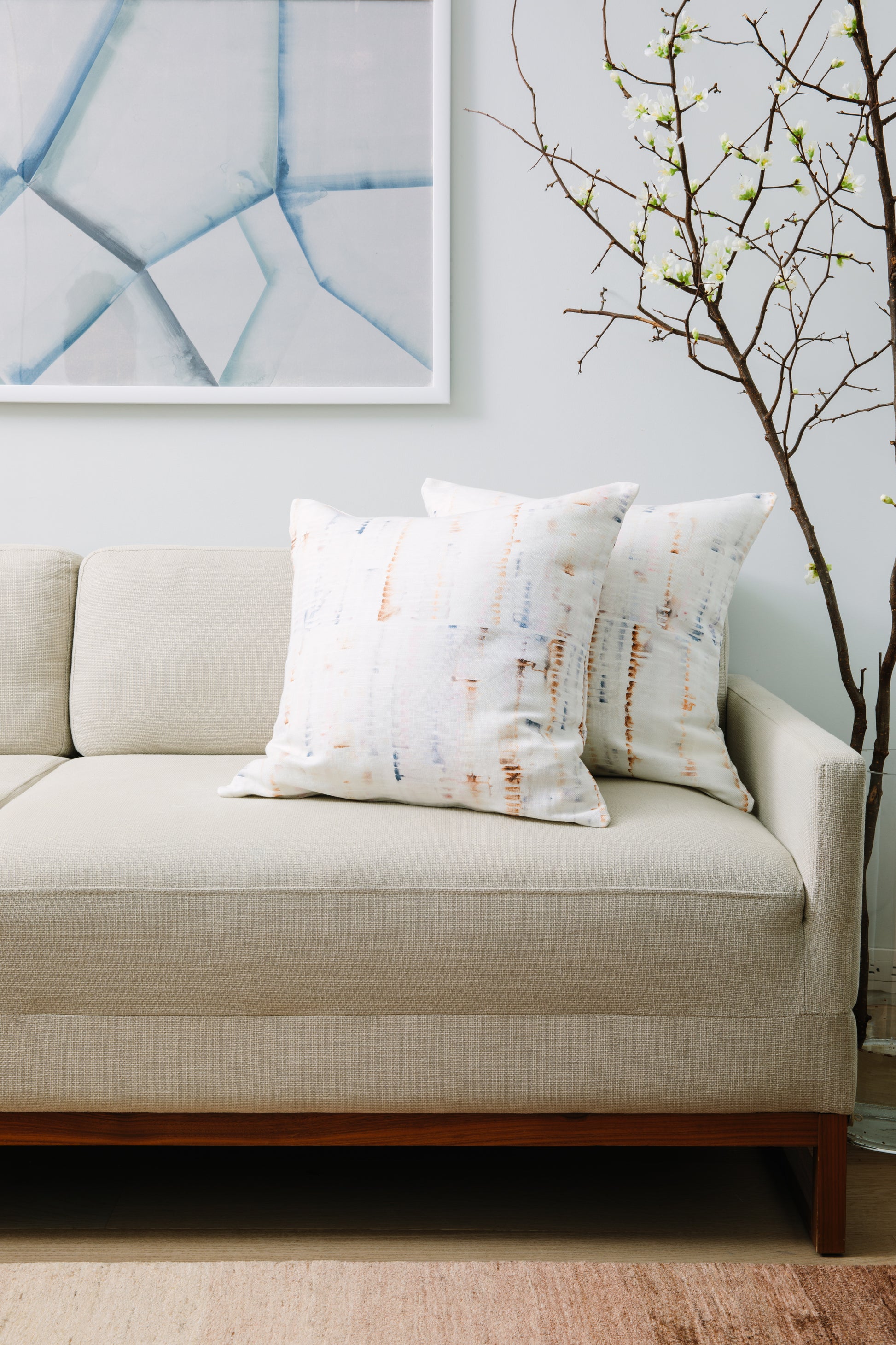 Beige sofa with patterned cushions against a light blue wall with abstract art.