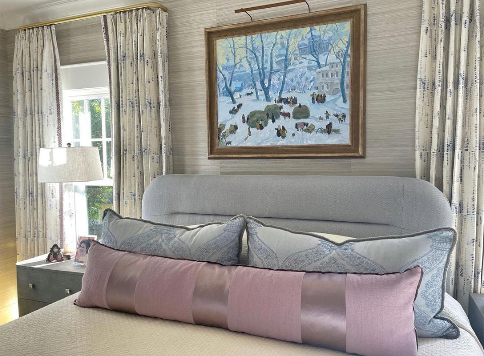 Decorative pillows on a bed with a framed painting on the wall in a bedroom setting.