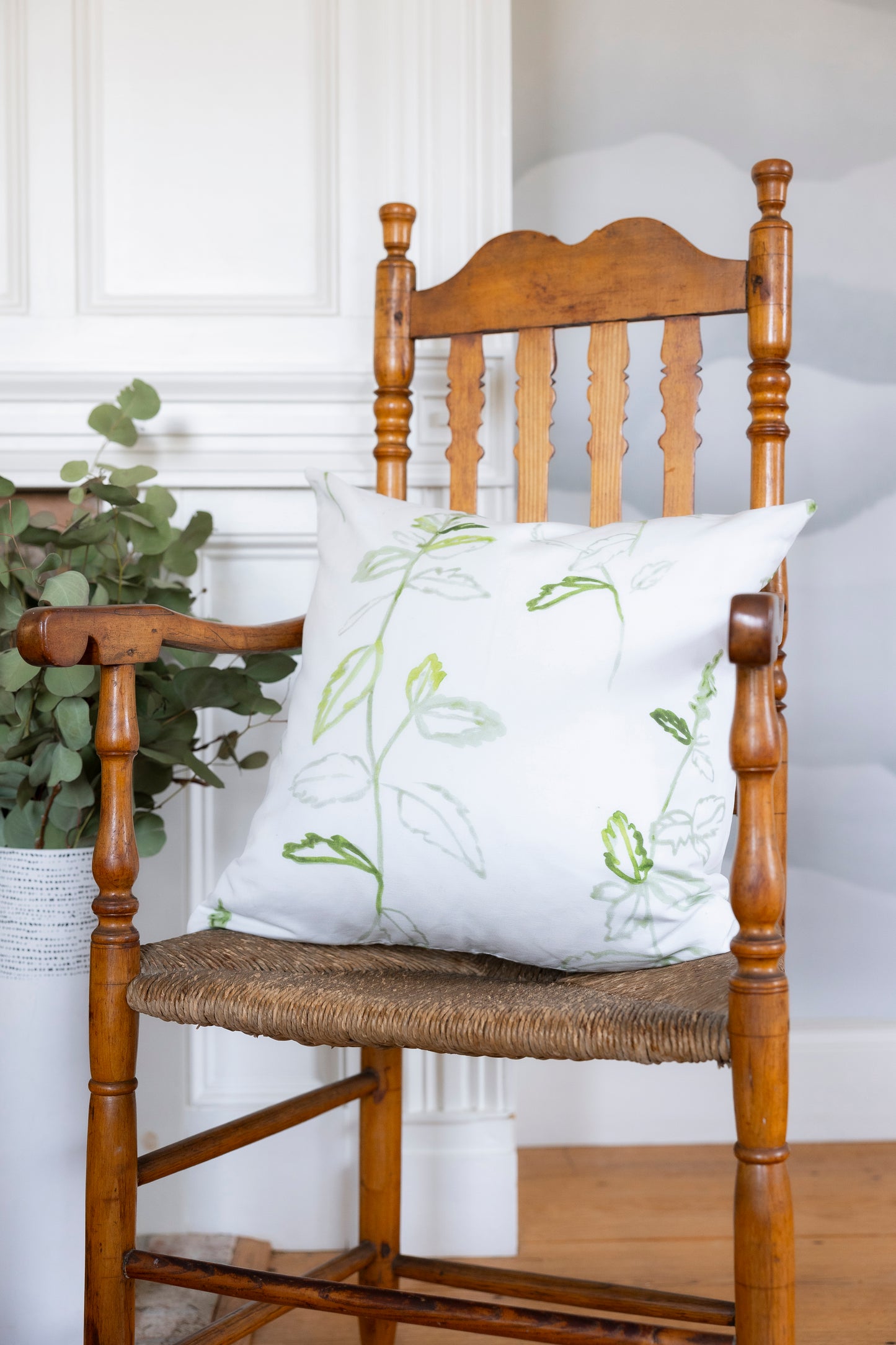 White pillow with green floral pattern on a wooden chair