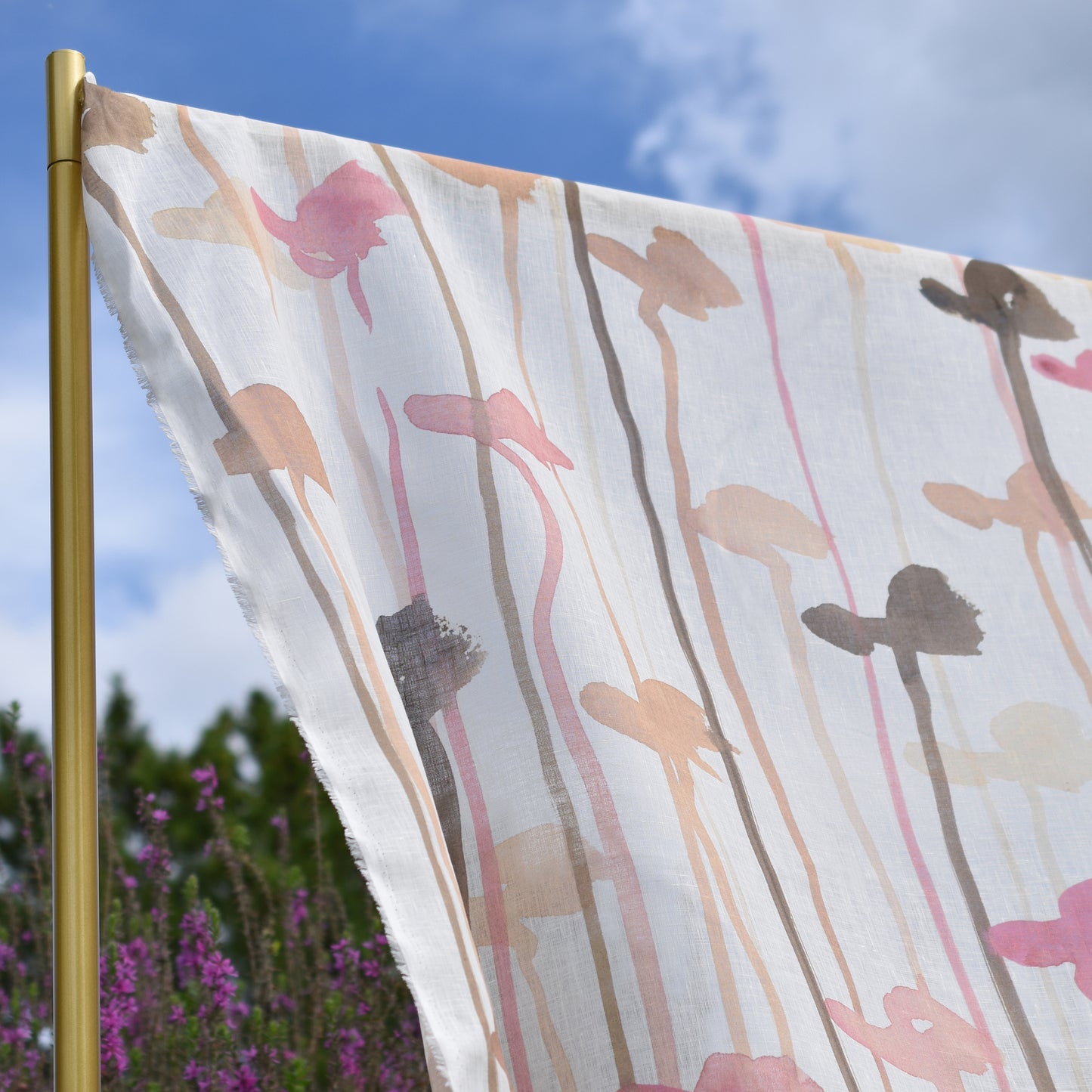 Floral-patterned fabric waving in the wind against a blue sky with trees and flowers in the background