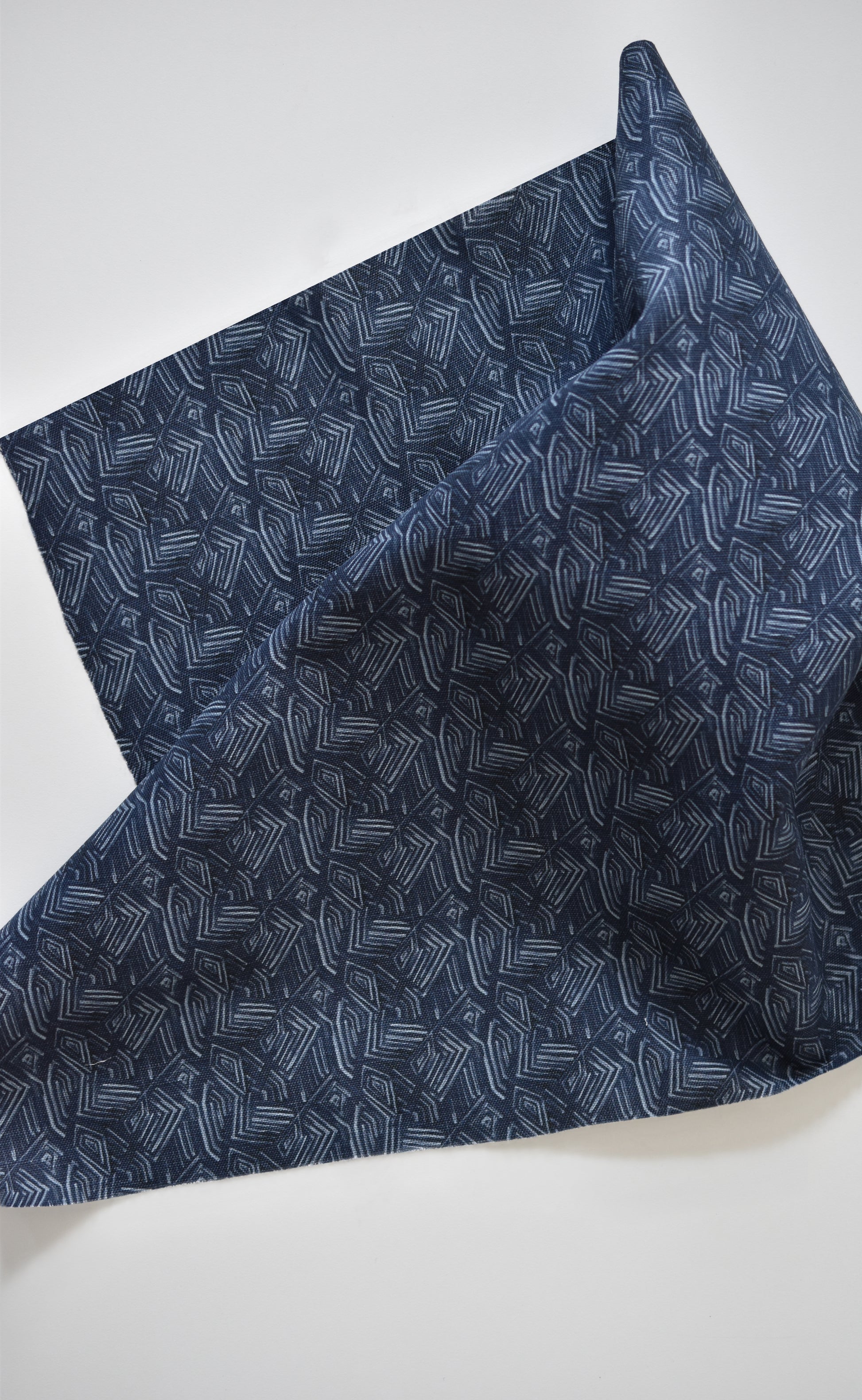Folded dark blue fabric with white geometric pattern on a light gray background