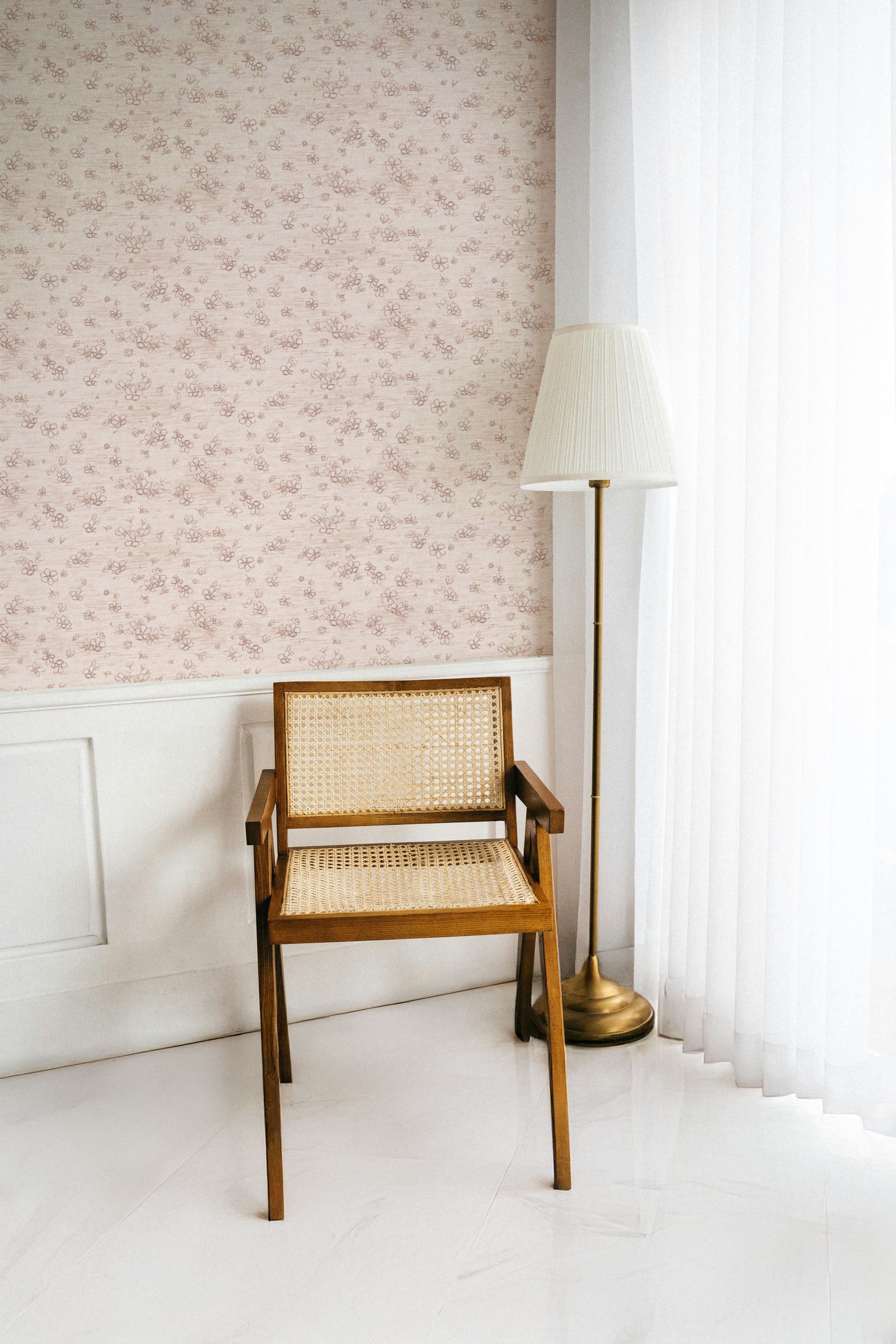 Wooden chair with wicker backrest against a light pink floral wallpapered wall.