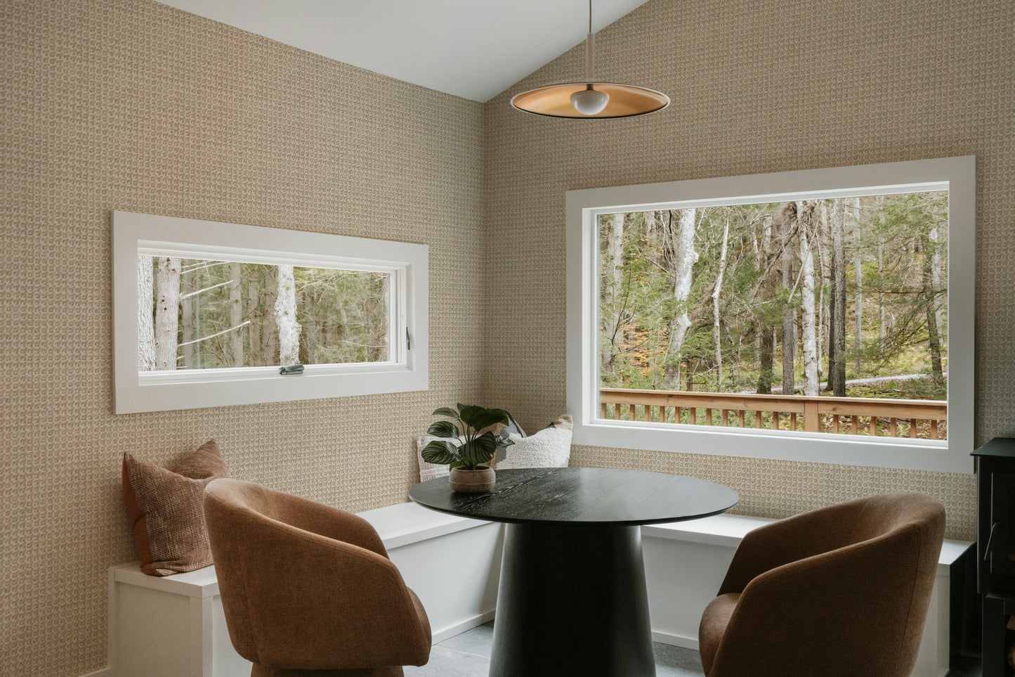 Modern dining room with a round table and chairs, featuring large windows with views of trees.