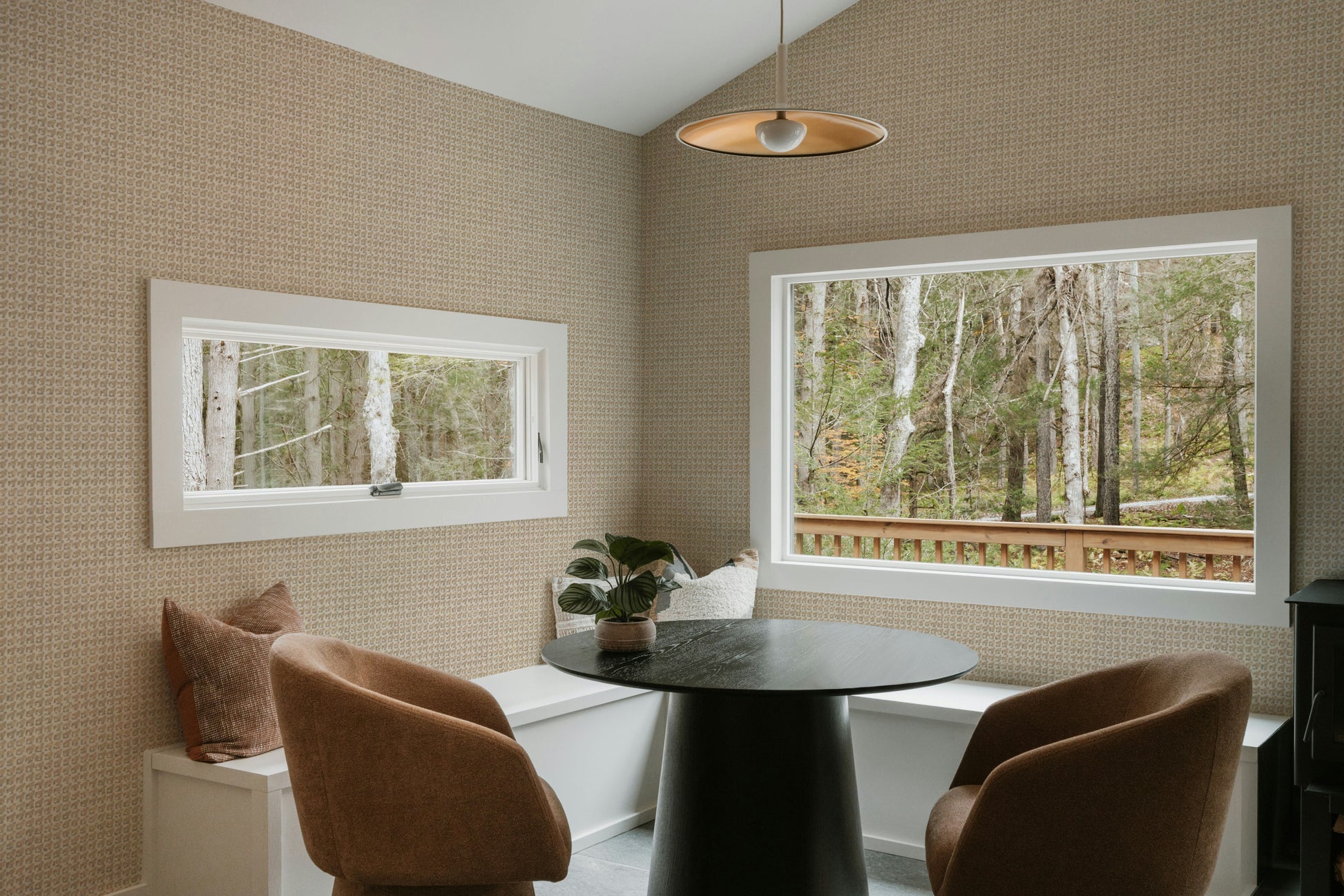 Modern dining room with a round table and chairs, featuring large windows with views of trees.